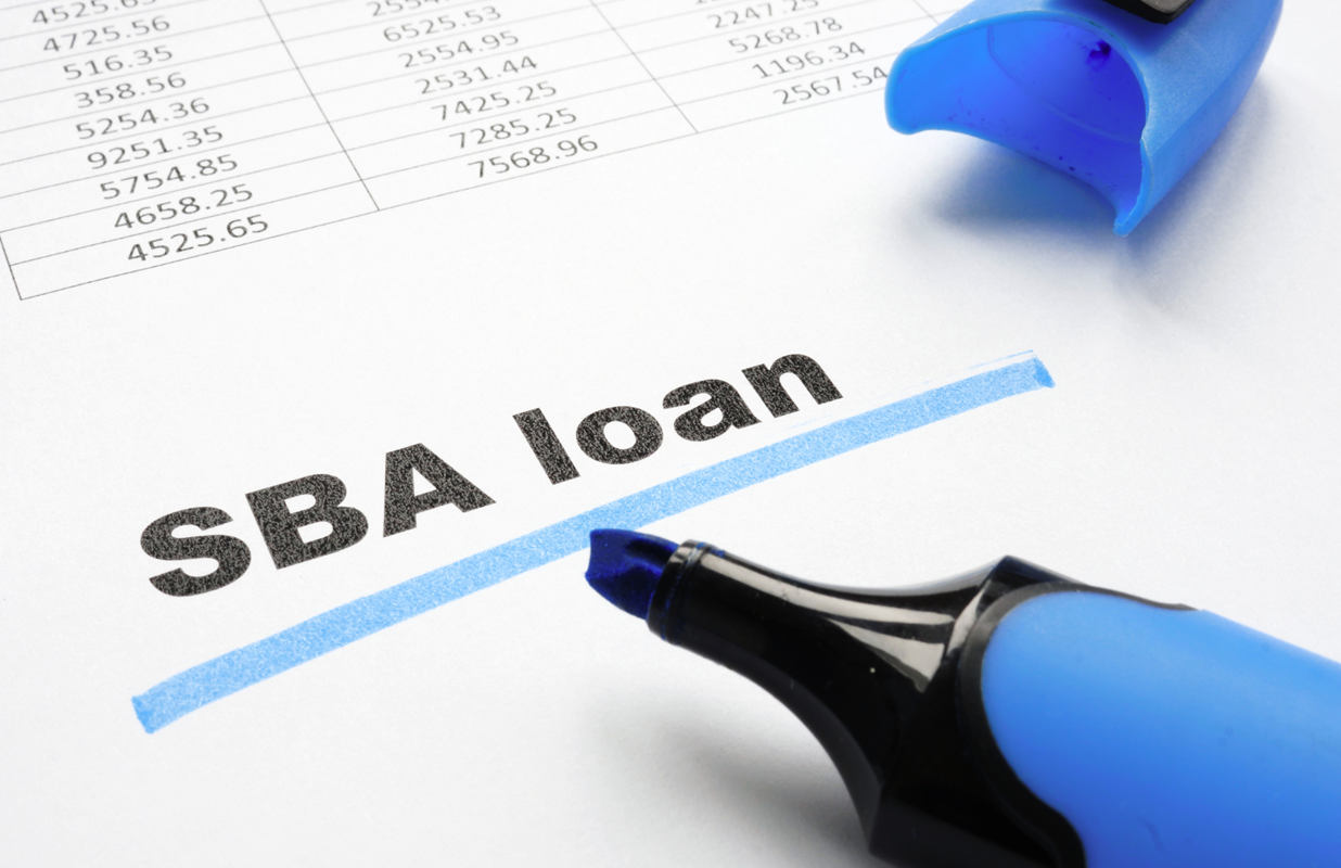 Blue highlighter resting next to the highlighted term 'SBA loan' on a white paper