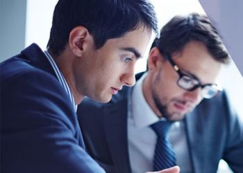 Two men in suits are talking intently, having a conversation in an office setting.